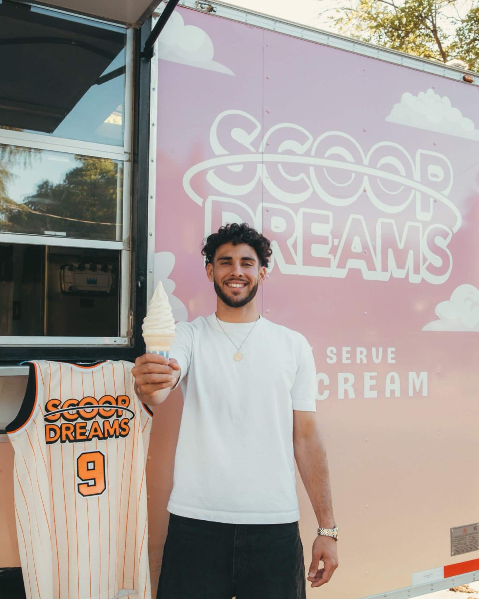 Devan Minouei holding a vanilla soft serve next to a hanging Scoop Dreams basketball jersey