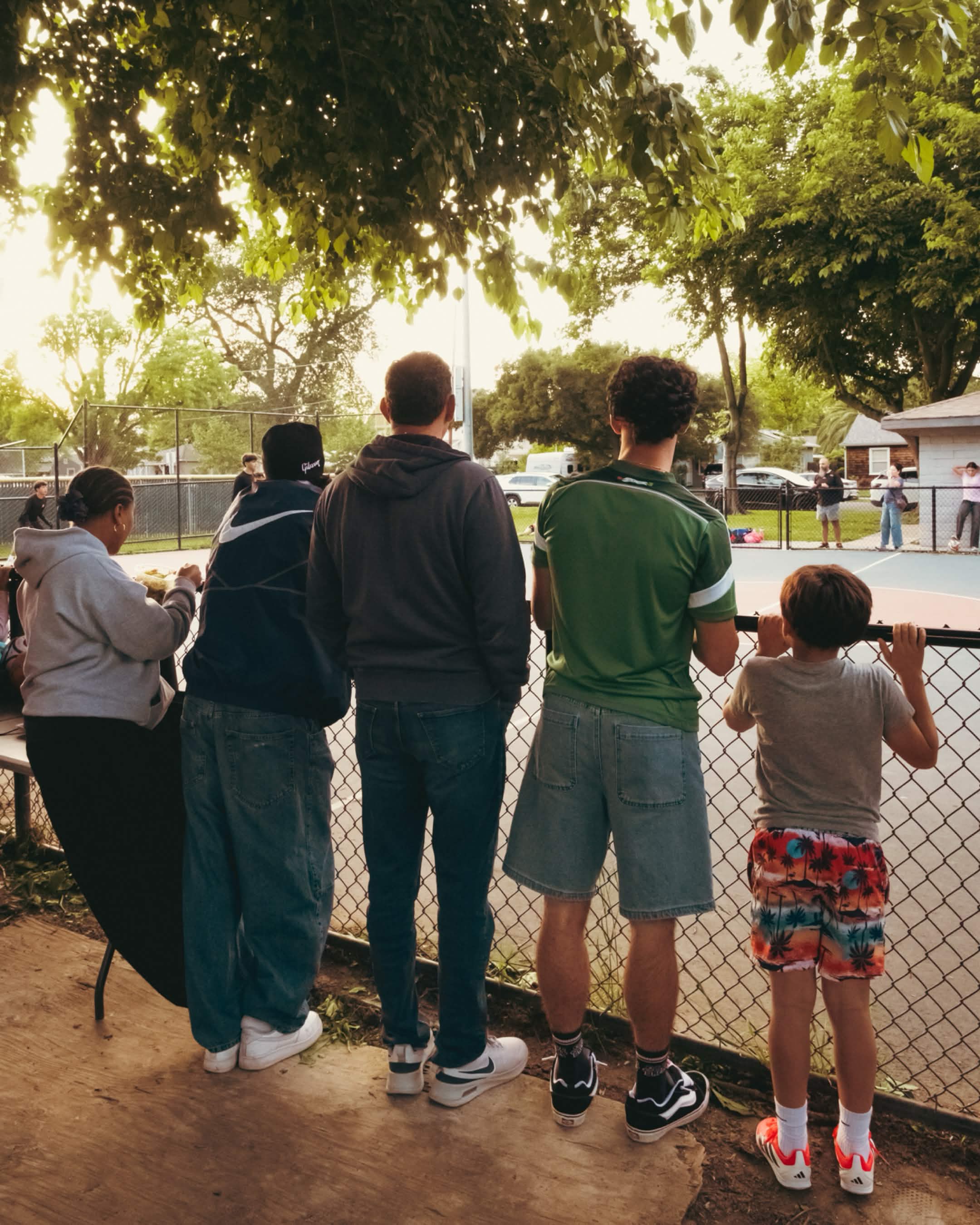 Spectators leaning on the chain-link fence watching the Scoop Dreams basketball tournament
